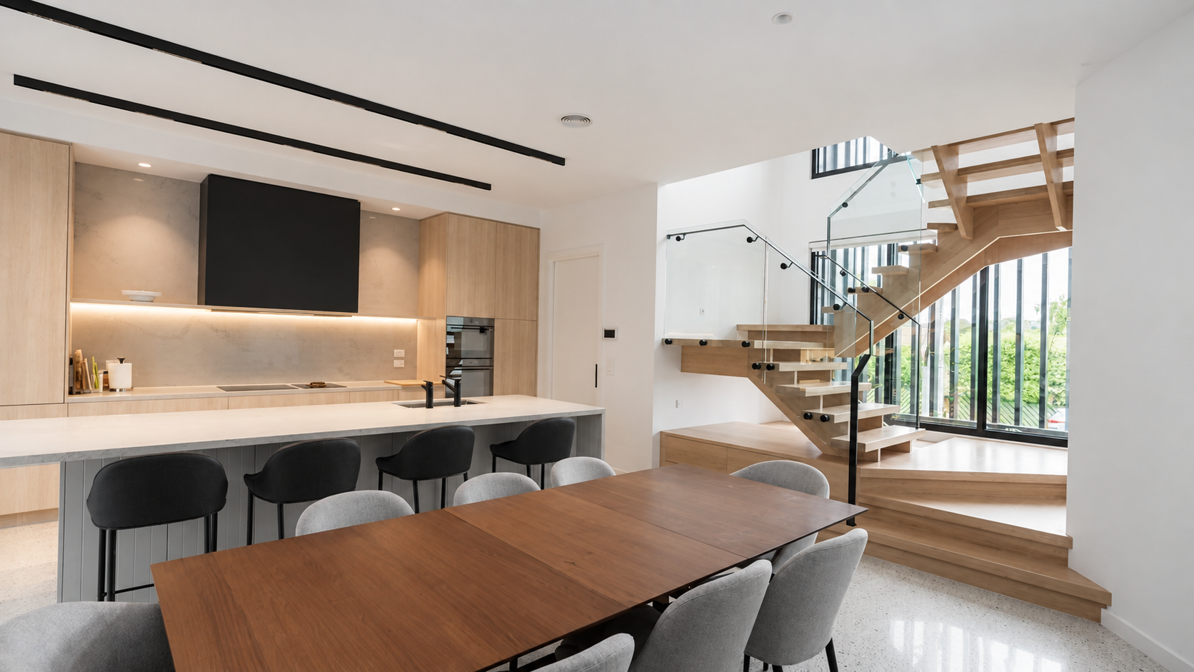 Kitchen and dining space with timber joinery, a floating staircase and full-height windows